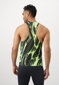 Top in rete di colore verde lime brillante e nero, caratterizzato da un motivo ondulato, design a schiena scoperta e schienale scoperto per una migliore ventilazione.