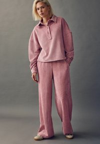 Helles rosa, geripptes Loungewear-Set mit langärmligem, geknöpftem Oberteil und locker sitzenden Hosen, aus weichem, strukturiertem Stoff gefertigt.