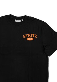 Schwarzes Baumwoll-T-Shirt mit orangefarbener, im geschwungenen Design bedruckter "SPRITZ CLUB"-Schrift auf der linken Seite der Brust. Kurze Ärmel.