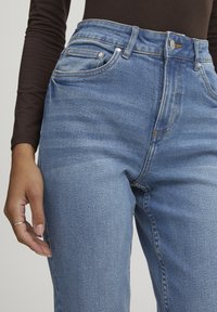 Jeans de mezclilla azul claros con un diseño de talle alto, que incluyen bolsillos delanteros, un ligero desvanecimiento y un cierre de botón en la cintura.
