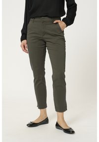 Pantalon tapered vert olive à taille haute, avec passants de ceinture, poches latérales et ourlets roulés. Associé à des ballerines en cuir verni noir.