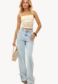 Kant crop top in off-white met verstelbare bandjes, gecombineerd met lichtblauwe hoge taille flared jeans met drawstring zoom en zijzakken.