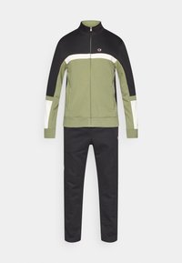 Survêtement vert olive, noir et blanc. Veste zippée avec col montant, manches longues, et pantalon assorti à jambes ajustées.