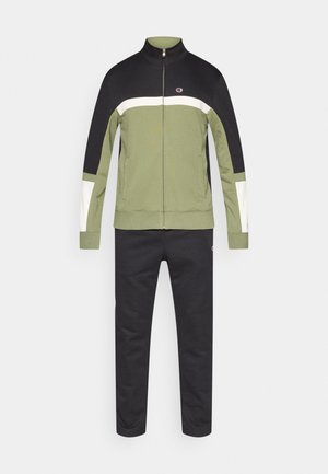 Sporta tērps olīvu zaļā, melnā un baltā krāsā. Žakete ar rāvējslēdzēju un augstu apkakli, garām piedurknēm, un atbilstošas bikses ar pieguļošām kājām.