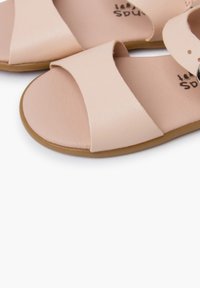 Vaaleanpunaiset sandaalit, joissa on leveät hihnat, litteät pohjat ja sileä pinta. Avoin varvasmuotoilu yksinkertaisella, minimalistisella ilmeellä.