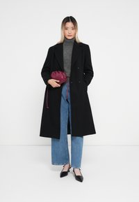Cappotto nero doppiopetto, dolcevita grigio, jeans azzurri a gamba larga, décolleté nere a punta e una piccola borsa a tracolla bordeaux.