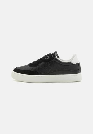 Baskets en cuir noir avec une surface texturée, accents blancs sur le talon et semelle en caoutchouc épaisse. Présente des lacets et un détail de logo en relief.