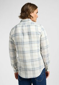 Herrskjorta med långa ärmar i rutigt mönster, vit med blå och gula rutor, knappade manschetter, avslappnad passform, mjukt tyg med subtil textur.