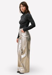 Zwarte top met lange mouwen gecombineerd met metallic zilverkleurige wijde broekspijpen. De broek heeft een hoge taille en zakken, met een gladde, glanzende textuur.