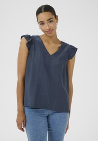 Haut bleu marine avec des manches courtes à volants, encolure en V et texture légère. Coupe simple et décontractée sans motifs ni accents.