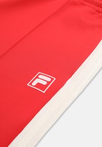 Rødt atletisk stof med hvid elastisk linning og Fila-logo broderet nær hvid tekstureret sidestribe.