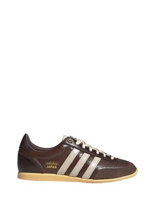 Bruine Adidas Japan sneaker met beige strepen, witte veters en gumzool, getoond in zijprofiel op witte achtergrond.