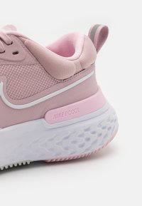 La sneaker Nike React rose présente un dessus texturé, des accents blancs, un col rembourré et une semelle en caoutchouc blanche avec un motif de grip.