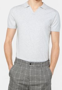 Camisa polo de manga corta color gris claro con cuello en pico, combinada con pantalones de cuadros grises con líneas blancas y detalles de botones.