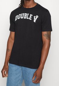 Černé bavlněné tričko s výrazným bílým nápisem "DOUBLE A" přes prsa. Kulatý výstřih a krátké rukávy s volným střihem.
