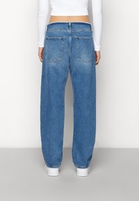 Blå denimjeans med en avslappnad passform, hög midja och bakfickor. Benen är uppvikta och de är kombinerade med vita sneakers.