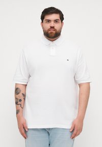 Valge polo särk krae ja kahe nupuga nööpimisega. Rinnal on väike logo. Kude paistab sile ja hingav.