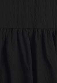 Svart tyg med en texturerad yta, med en slät övre del och en samlad, flödande nedre del. Enkelt design med minimal detaljering.