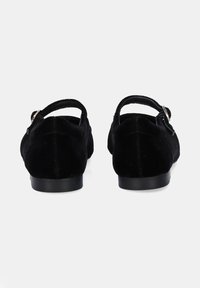 Zapatos de terciopelo negro con tacón bajo, punta cuadrada y una correa ajustable. Textura suave con acabado mate y diseño minimalista.