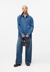 Tamno plava traper košulja s džepom i detaljem s logotipom. Široke traperice u sličnom denimu, uparene s malom crnom torbicom i masivnim crnim čizmama.