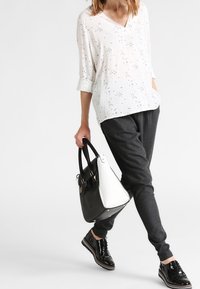 Blusa blanca con lunares, escote en V, mangas remangadas; pantalones deportivos gris oscuro; bolso negro y blanco; zapatos negros con cordones y acabado brillante.