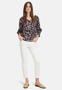 Maglietta nera con motivo geometrico astratto rosa e bianco, vestibilità rilassata, scollo a barca, maniche lunghe. Abbinata a pantaloni bianchi in vestibilità slim e mocassini beige.