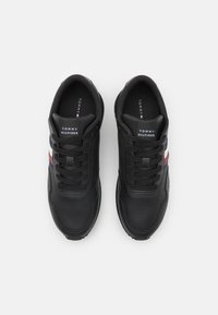 Sneakers in pelle nera con punta arrotondata e dettagli in rete. Il design presenta strisce rosse e blu sui lati e un'etichetta con il marchio sulla linguetta.