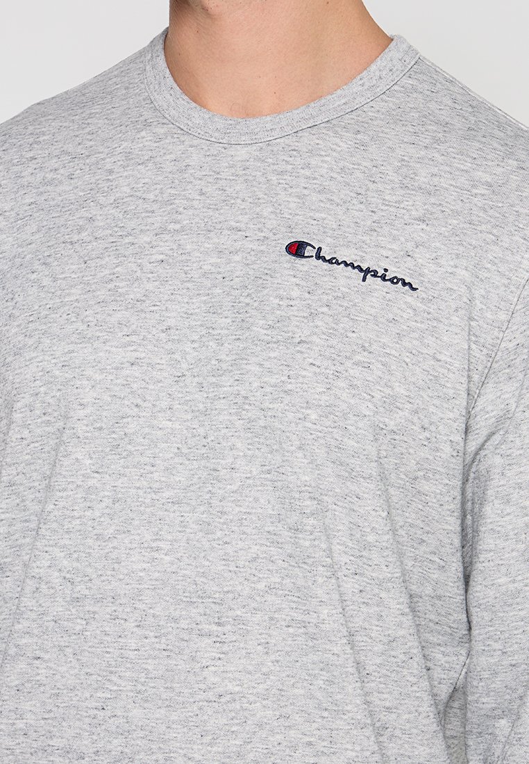 T-shirt in cotone grigio con scollatura rotonda e maniche corte, con il logo "Champion" ricamato in blu navy sul lato sinistro del petto.