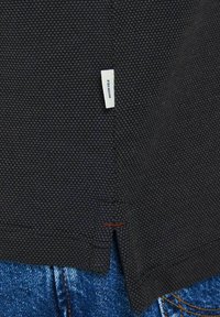 Short-sleeve black textured shirt with a side slit detail, featuring a white label reading "PREMIUM" and contrasting red stitching.