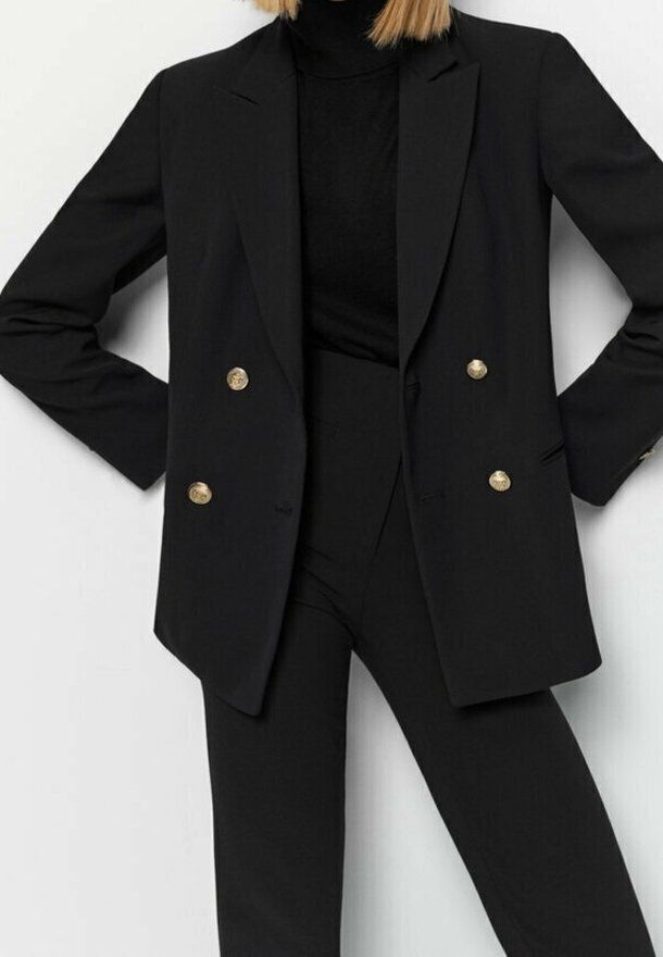 Blazer noir à double boutonnage avec des boutons dorés, associé à un col roulé noir, présentant une coupe ajustée et une texture de tissu lisse.