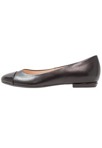 Scarpa piatta in pelle nera con una punta rotonda lucida nera e un tacco basso, mostrata in profilo laterale su uno sfondo bianco.