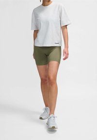 Camiseta gris de manga corta y pantalones cortos ajustados verdes oliva de tela elástica, combinados con zapatillas deportivas grises claras.