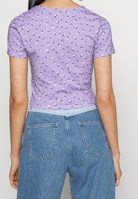 Ljuslila kortärmad topp med blommönster; figurnära design. Bärs med högmidjade blå denimjeans med bakfickor.