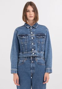 Középkék farmerdzseki, cropped fazonnal, gombos elülső záródással, két mellzsebbel és klasszikus gallérral. Sima textúra és varrási részletek.