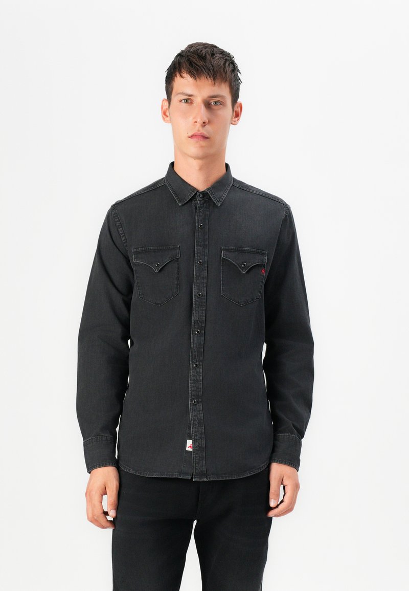 Zwarte denimhemd met knoopsluiting aan de voorkant, twee borstzakken en een rode logo-accent. Kenmerkt zich door een klassieke kraag en lange mouwen.
