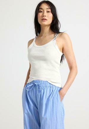Hvid ribbet tanktop parret med lyseblå stribede bukser med snoretræk, der har sidelommer og blødt, let stof.