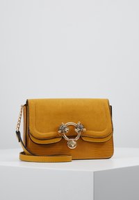 Borsa a tracolla in suede gialla con base testurizzata, dotata di una catena dorata e di una chiusura circolare decorata con dettagli a forma di testa di leopardo.