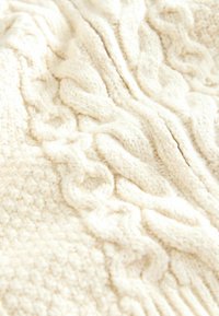 Tejido de punto grueso en crema con patrones de cable texturizados y una apariencia suave y esponjosa, mostrando detalles de zigzag y acanalados en todo su recorrido.