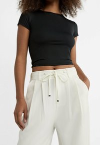 Zwarte korte mouwen crop top gecombineerd met witte hooggewaisted geplooide broek met een trekkoord in de taille en metallic accenten.