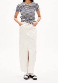 Randig kortärmad skjorta tillsammans med en lång vit denimkjol med en framfåra, kompletterad med svarta platåskor och vita strumpor.