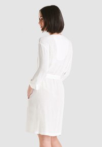 Ropa blanca texturizada con mangas largas y un cinturón a juego. Presenta bolsillos laterales y un diseño de espalda en forma de scoop.