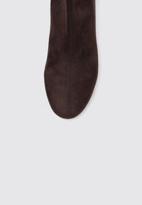 Bottine en suède marron avec une texture lisse, un orteil rond et de subtils détails de couture le long de la couture. Présentée sur un fond clair.