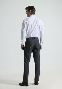 Atuendo masculino que incluye una camisa de vestir blanca ajustada con una textura suave y pantalones grises a medida, combinados con zapatos negros.