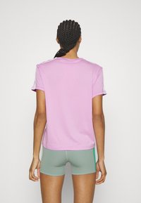 Camiseta de manga corta rosa con cuello redondo y franjas blancas en los hombros, combinada con pantalones cortos verdes. Textura de algodón suave.