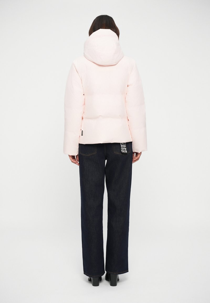 Veste doudoune rose pâle avec capuche, dotée d'un design matelassé. Associée à un pantalon large en denim foncé et à des bottes à talons noires.