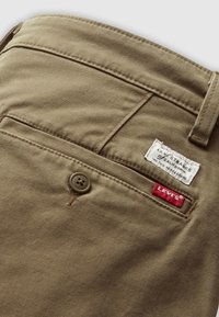 Beige cotton pants with a textured finish. Features a back pocket with a Levi's label and a button closure with embossed details.