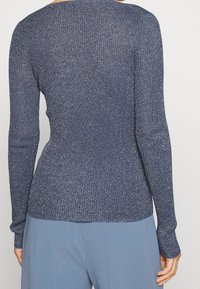 Haut à manches longues côtelé bleu marine avec détails scintillants métalliques. Coupe ajustée mettant en valeur la silhouette, doté d'un col rond et d'un tissu extensible.