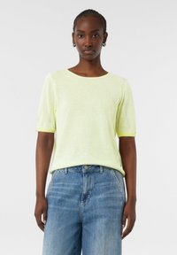 Limoengroen gestreept gebreid topje met korte mouwen, ronde hals en een losse fit, gecombineerd met lichtblauwe denim jeans. Zachte textuur en casual ontwerp.