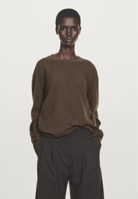 Brun, överdimensionerad tröja gjord av mjukt material med rund halsringning. Kombinerad med mörka, veckade byxor som skapar en avslappnad silhuett.