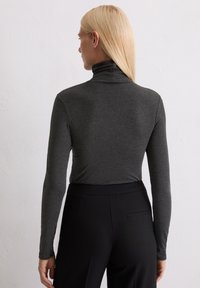 Langärmliges Rollkragenshirt in Dunkelgrau, aus glattem Stoff mit taillierter Silhouette, kombiniert mit schwarzen Hosen, von hinten gezeigt.